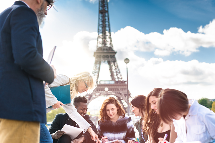 Happy students studying abroad France writing in outdoors.